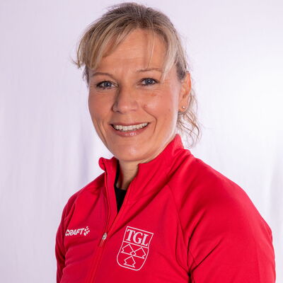 Eine lächelnde Frau trägt eine rote TGL-Jacke, symbolisierend den Sportgeist des Vereins Turngemeinde Landshut.