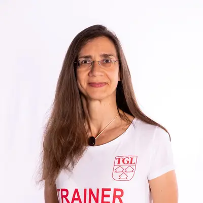 Eine Frau im TGL-Trainer-Shirt der Turngemeinde Landshut lächelt freundlich in die Kamera.