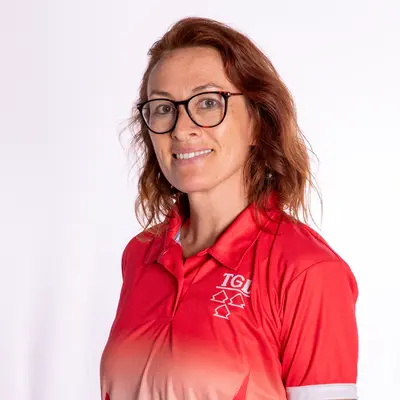 Eine Frau in einer roten Jacke mit dem TGL-Logo lächelt freundlich in die Kamera.