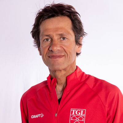 Eine lächelnder Mann trägt eine rote TGL-Jacke, symbolisierend den Sportgeist des Vereins Turngemeinde Landshut.