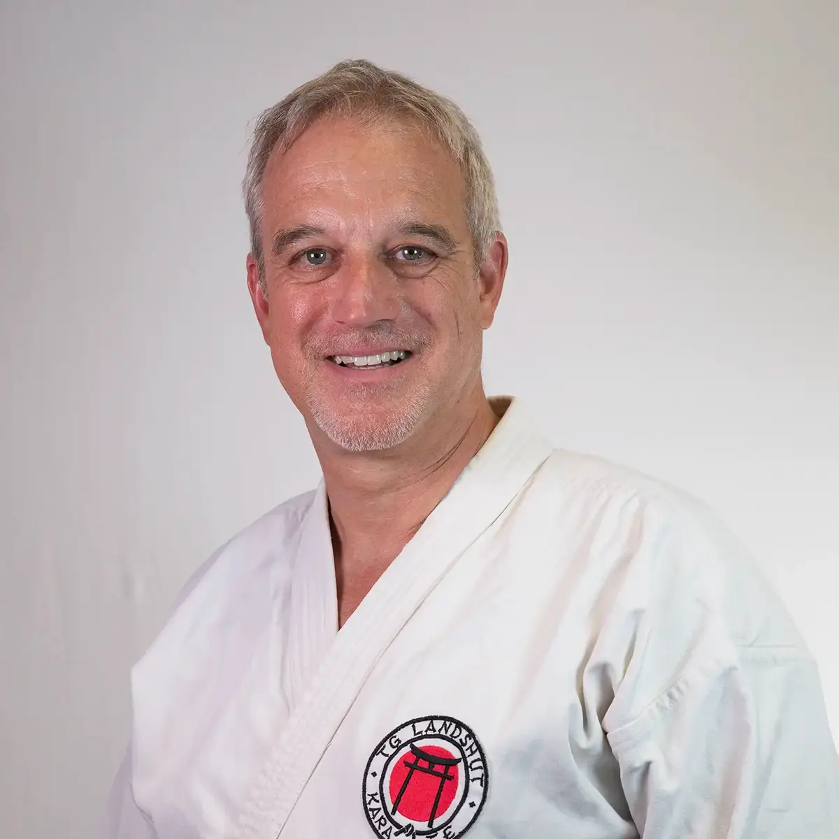 Ein Mann in Karateanzug mit dem Logo der TG Landshut lächelt freundlich in die Kamera.