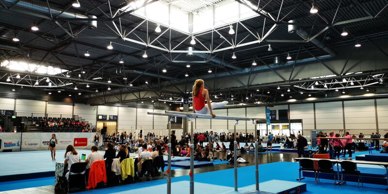 Ein Turner der Turngemeinde Landshut zeigt eine beeindruckende Übung am Barren in einer großen Sporthalle.