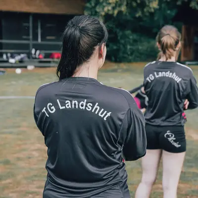 Zwei Sportlerinnen in TG Landshut-Trikots stehen auf einem Rasenplatz, bereit für ein Training des Vereins.
