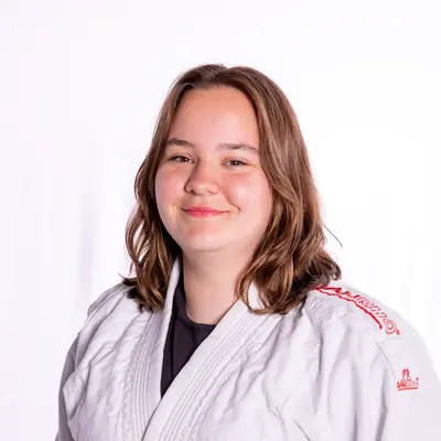 Eine junge Person in einem weißen Judoanzug lächelt selbstbewusst und repräsentiert den Sportverein Turngemeinde Landshut.