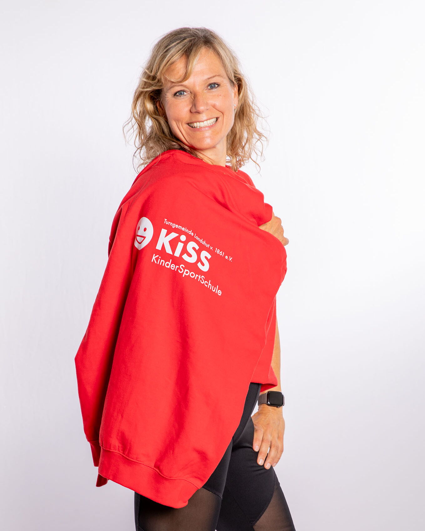 Eine Frau in einem roten KiSS-Pullover lächelt und repräsentiert stolz den Sportverein Turngemeinde Landshut.