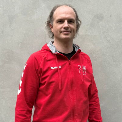 Ein Mann in einem roten TGL-Trikot schaut in die Kamera, stolz seinen Sportverein Turngemeinde Landshut repräsentierend.