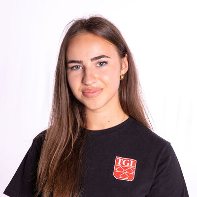 Eine junge Frau lächelt in einem TGL-T-Shirt, das den Sportverein Turngemeinde Landshut repräsentiert.