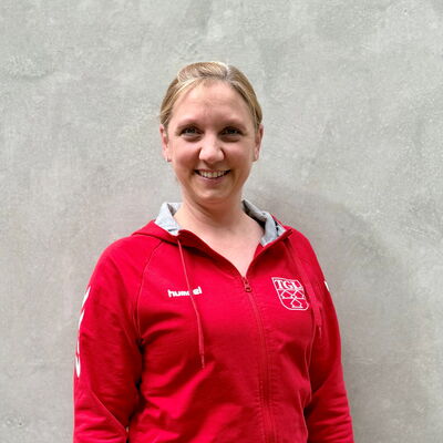 Eine Frau in einem roten TGL-Trikot lächelt in die Kamera, stolz ihren Sportverein Turngemeinde Landshut repräsentierend.