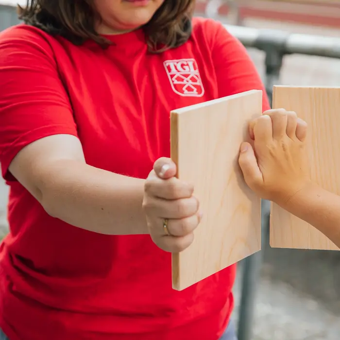 Eine Person im roten TGL-Shirt hält Bretter, während eine andere Person sie mit einer Hand schlägt, um Sport zu demonstrieren.
