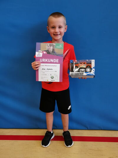 Ein Junge namens Artur hält stolz eine Urkunde und ein Spielzeugauto bei einem Sportereignis der Turngemeinde Landshut.