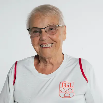 Eine Frau im TGL-Trainer-Shirt der Turngemeinde Landshut lächelt freundlich in die Kamera.