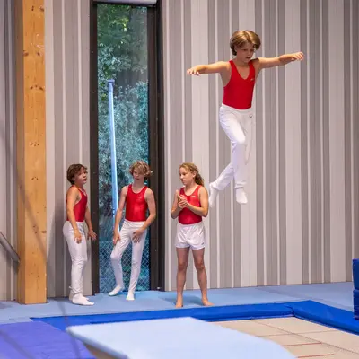 Ein Turner der Turngemeinde führt auf dem Trampolin einen Sprung aus, während drei Kinder zuschauen.