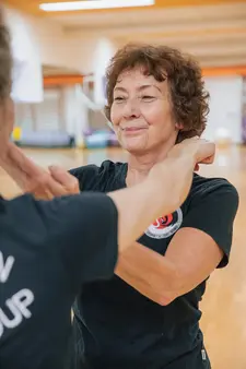 Eine Frau in einem Trainingsraum der Turngemeinde Landshut übt mit einem Partner eine sportliche Bewegung.