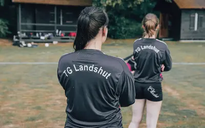 Zwei Sportlerinnen in TG Landshut-Trikots stehen auf einem Rasenplatz, bereit für ein Training des Vereins.