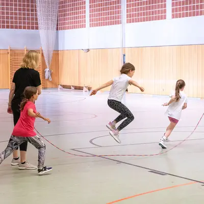 Kinder springen in einer Turnhalle der Turngemeinde Landshut beim Seilspringen unter Anleitung eines Trainers.
