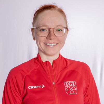 Eine lächelnde Frau trägt eine rote TGL-Jacke, symbolisierend den Sportgeist des Vereins Turngemeinde Landshut.