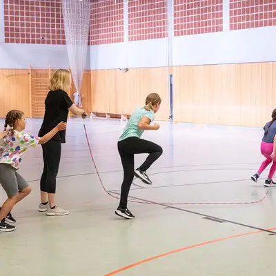 Kinder und ein Trainer springen über ein Seil in einer Sporthalle der Turngemeinde Landshut.