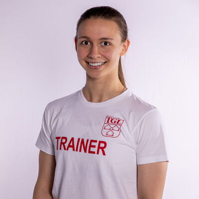 Eine Frau in einem T-Shirt mit TGL-Logo lächelt freundlich, als Trainerin des Vereins Turngemeinde Landshut.