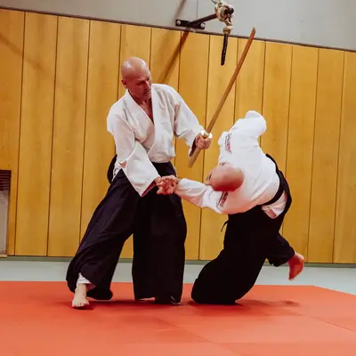 Zwei Männer üben Aikido-Techniken in einem Dojo der Turngemeinde Landshut auf einer roten Matte.