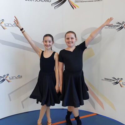 Zwei junge Tänzerinnen in schwarzen Kleidern posieren stolz beim Tanzsportwettbewerb für den Verein Turngemeinde Landshut.