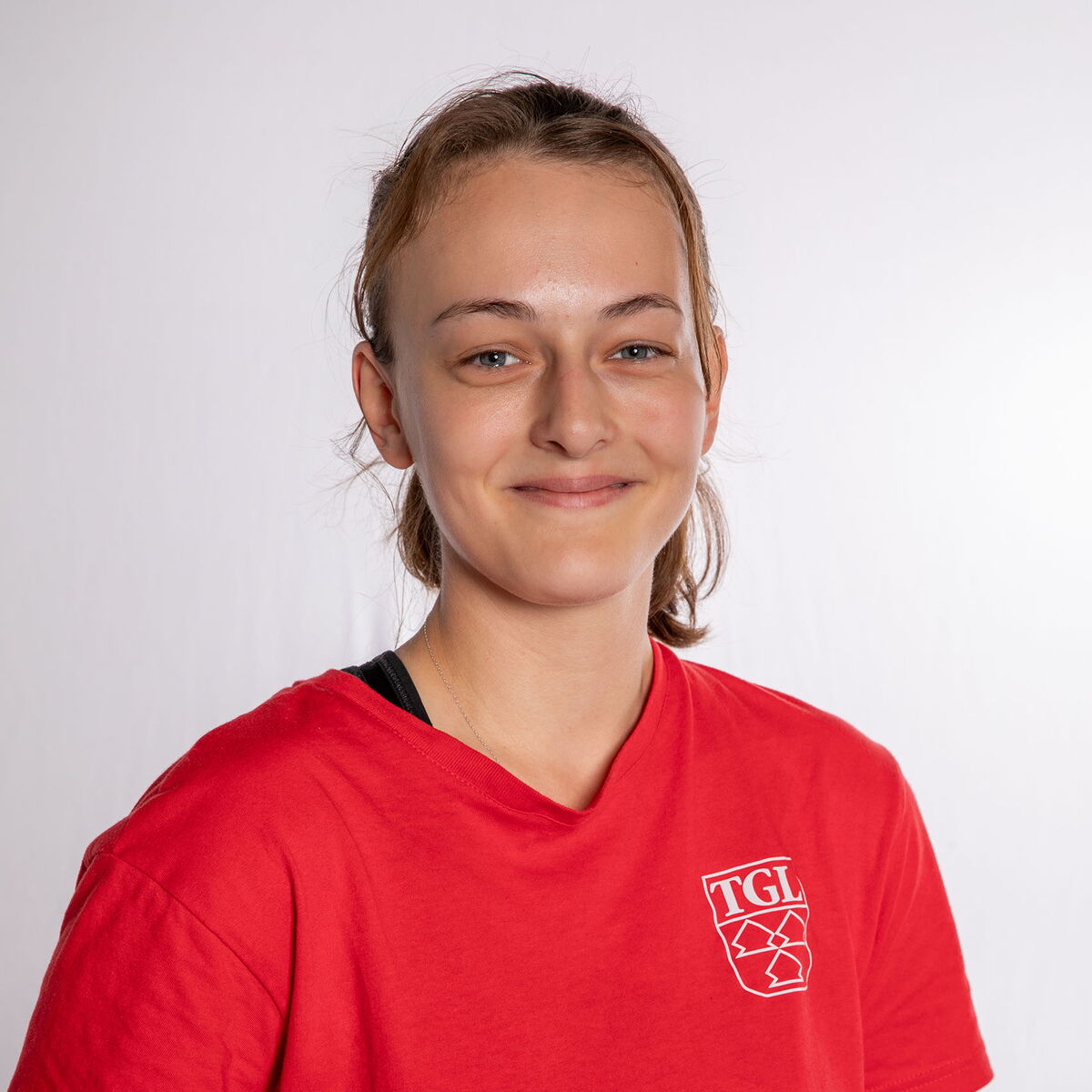 Eine junge Frau im roten TGL-Shirt lächelt freundlich in die Kamera, repräsentativ für den Verein in Landshut.