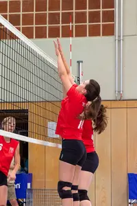 Spielerinnen des Vereins TG Landshut blocken einen Volleyball am Netz in einer Sporthalle.