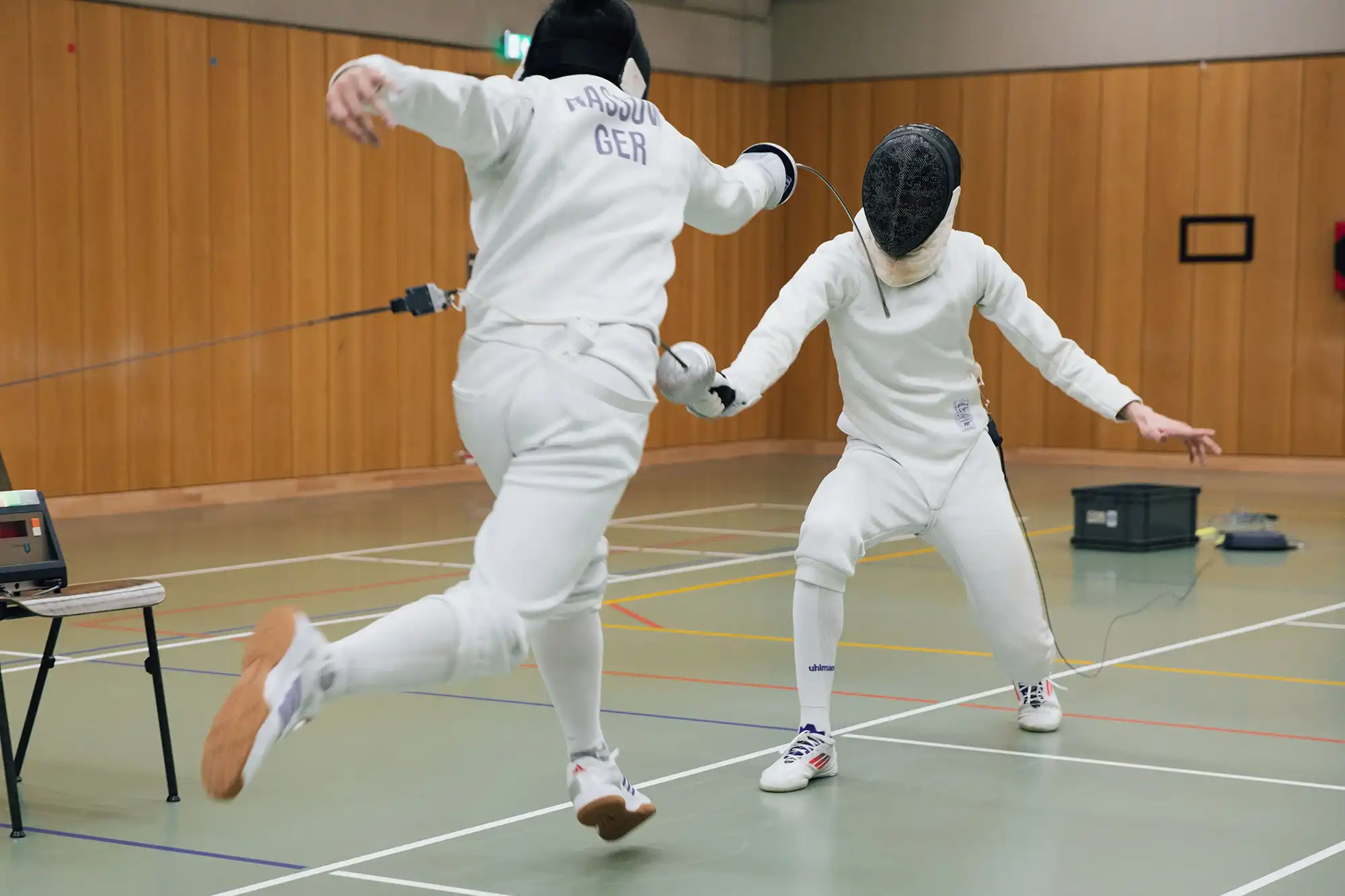 Zwei Fechter der Turngemeinde Landshut sind in einem dynamischen Gefechtsmoment auf der Sporthalle zu sehen.
