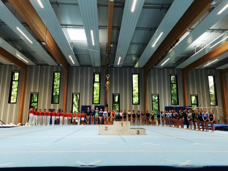 Athleten der Turngemeinde Landshut stehen bei der Vereinsmeisterschaft aufgereiht vor dem Siegerpodest in der Sporthalle.