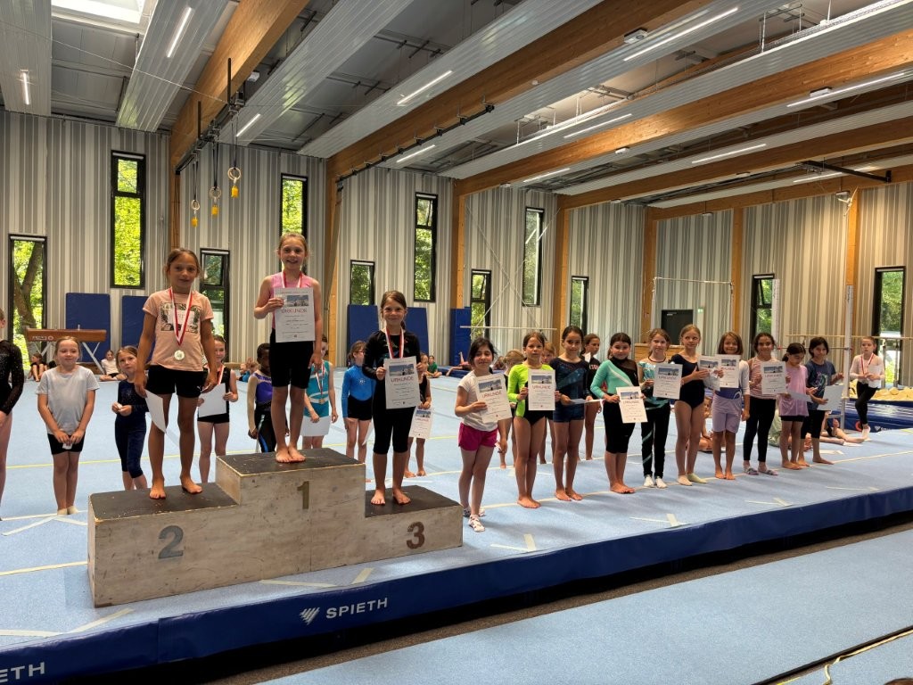 Kinder stehen auf einem Siegertreppchen und halten Urkunden bei einem Turnwettbewerb der Turngemeinde Landshut.