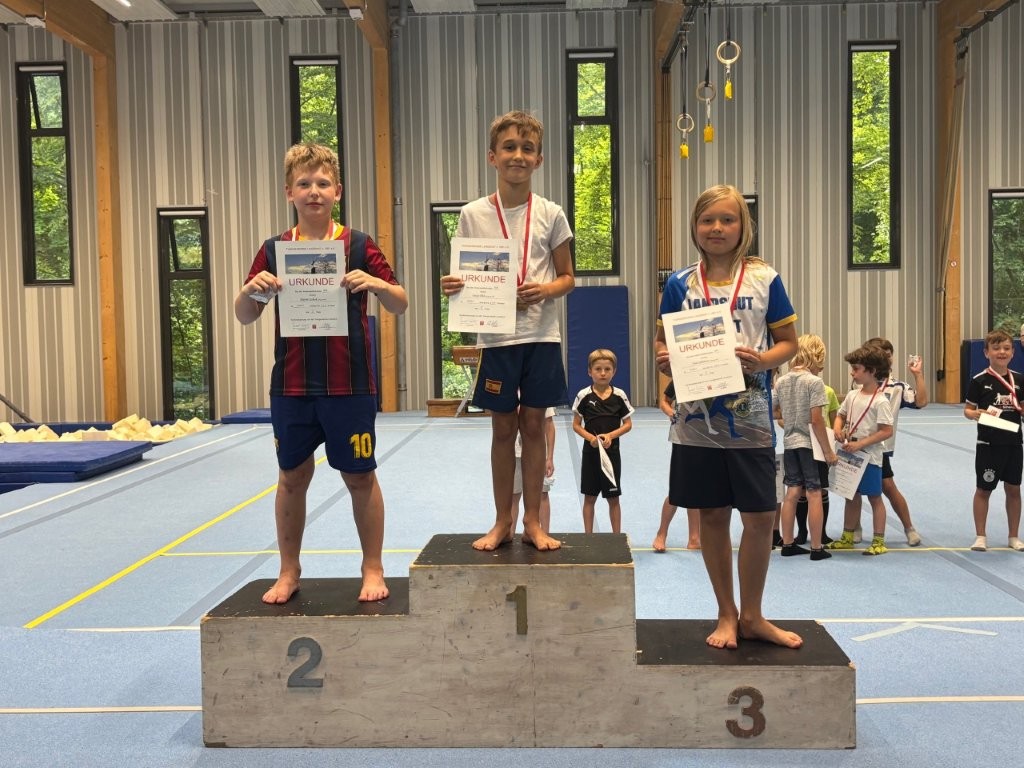 Drei Jungen stehen auf einem Podest und halten Urkunden bei einem Turngemeinde Landshut Sportwettbewerb.