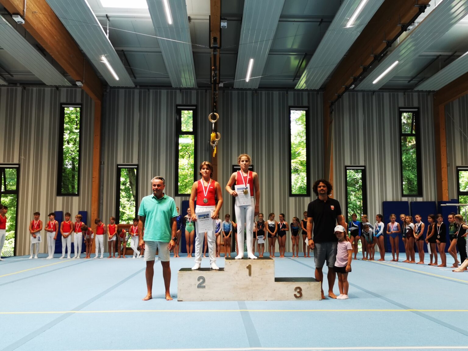 Junge Sportler stehen auf dem Siegerpodest bei einem Turnier der Turngemeinde Landshut in einer Sporthalle.