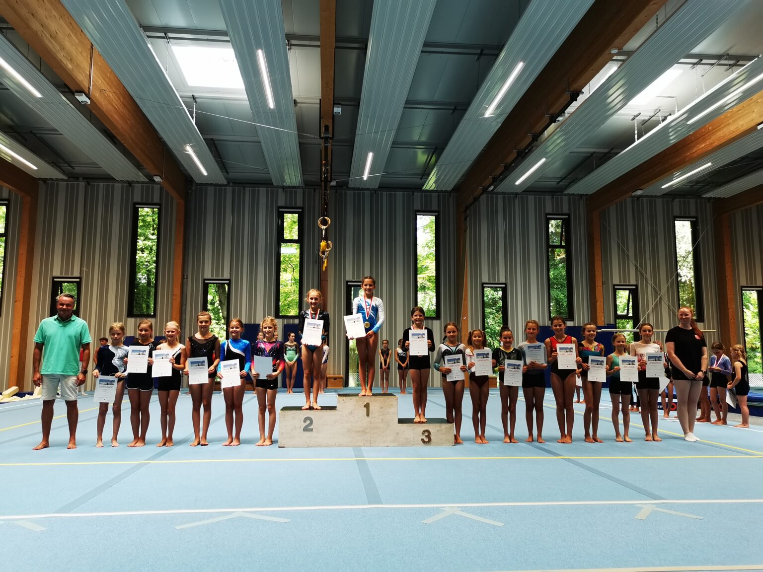 Eine Gruppe von Mädchen steht in einer Sporthalle der Turngemeinde Landshut auf einem Podium und hält Urkunden.