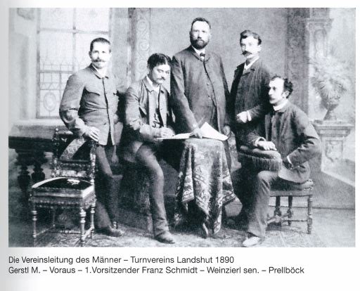 Fünf Männer des Turnvereins Landshut posieren 1890 im Vereinsvorstand mit einem Tisch im Zentrum.